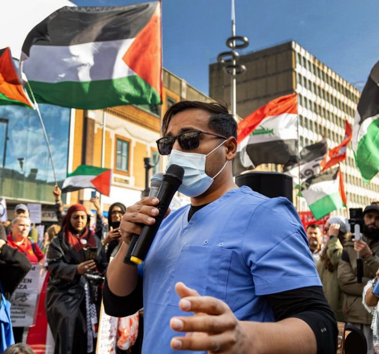Dr Ahmed Alshantti speaking at a Palestinian event in Cardiff with crowds and flags in the background